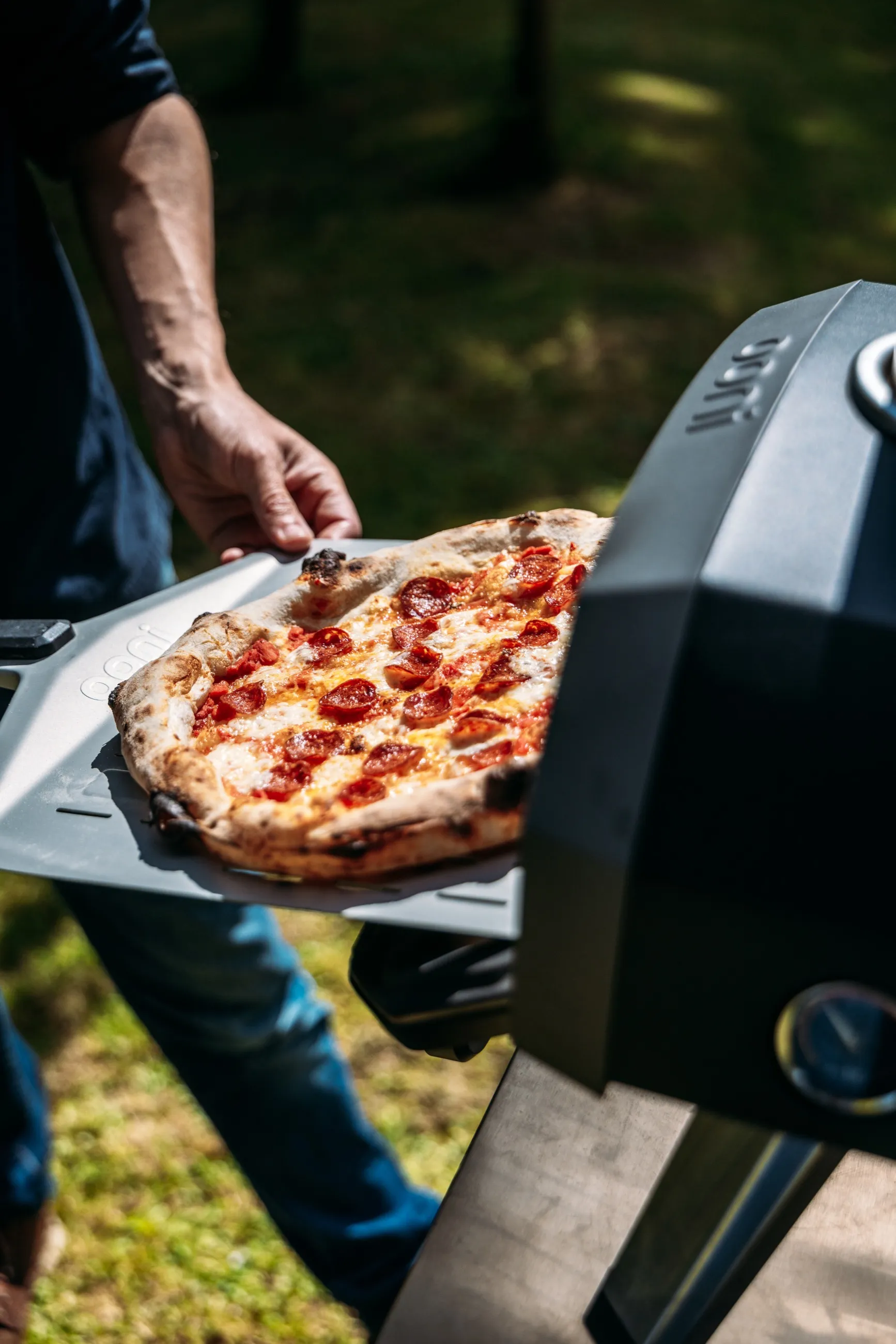 Pepperoni pizza being placed in an outdoor pizza oven